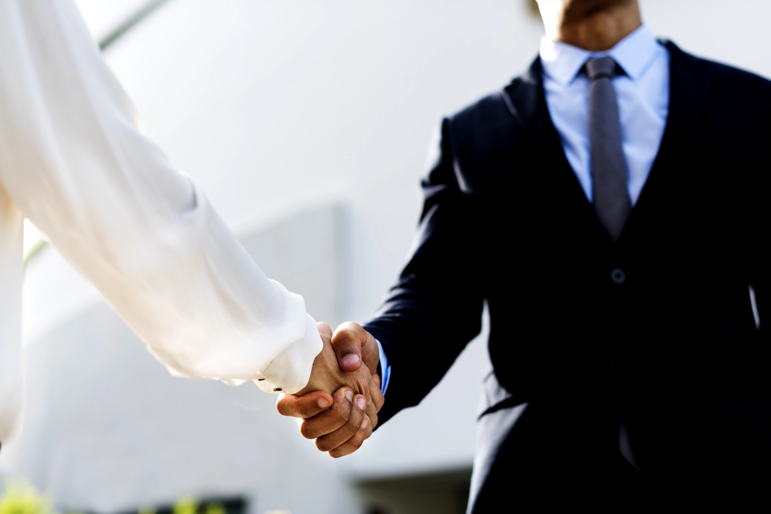 Mes West GmbH - Fachkräfte-, Investitions- und Unternehmenslösungen - Nahaufnahme eines Geschäftsmannes in dunklem Anzug, hellblauem Hemd und Krawatte, der die Hand zum Händeschütteln ausstreckt.