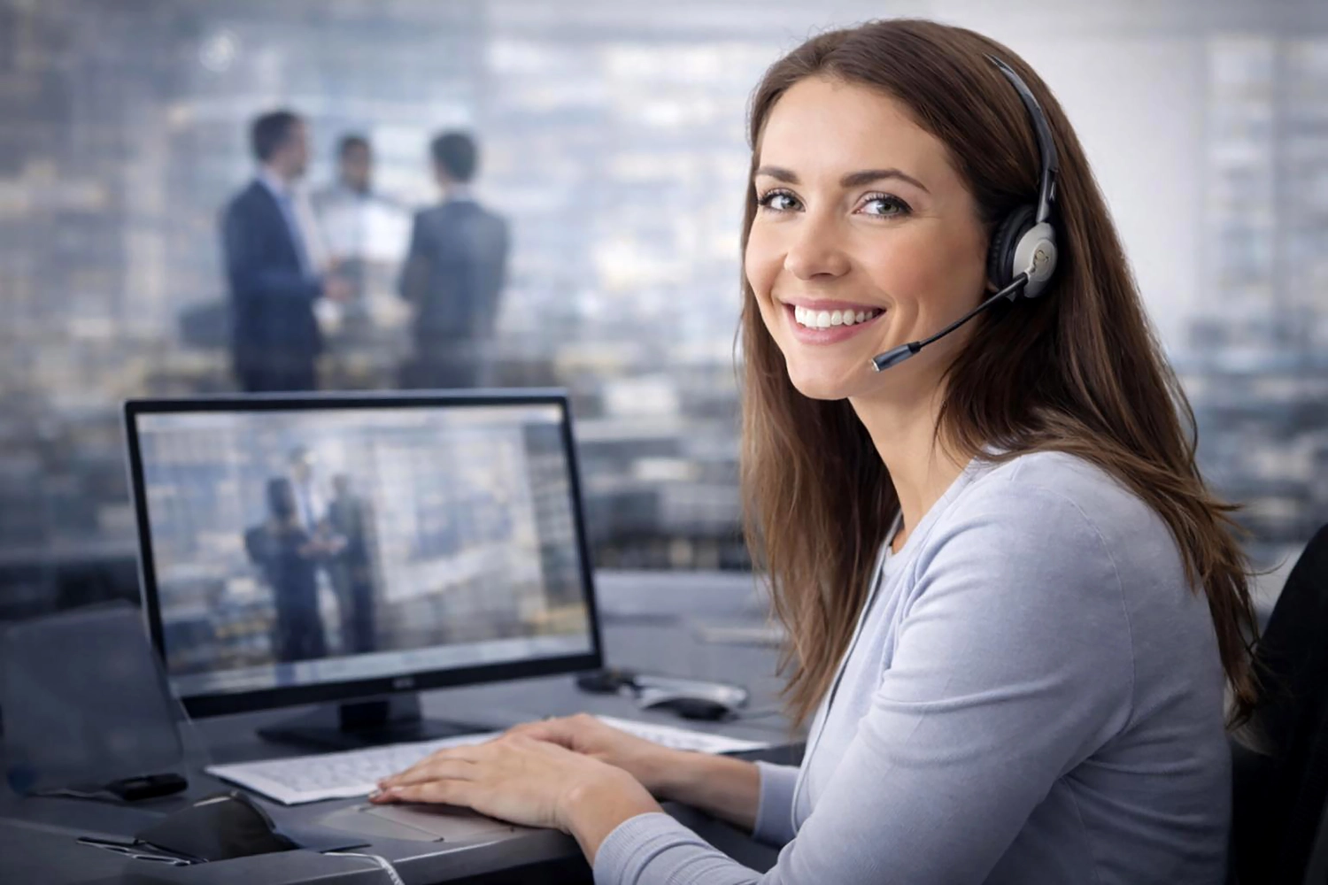 Mes West GmbH - Fachkräfte-, Investitions- und Unternehmenslösungen - Ein Büroangestellter mit Headset lächelt vor einem verschwommenen Hintergrund von Kollegen in einem Bürogebäude.