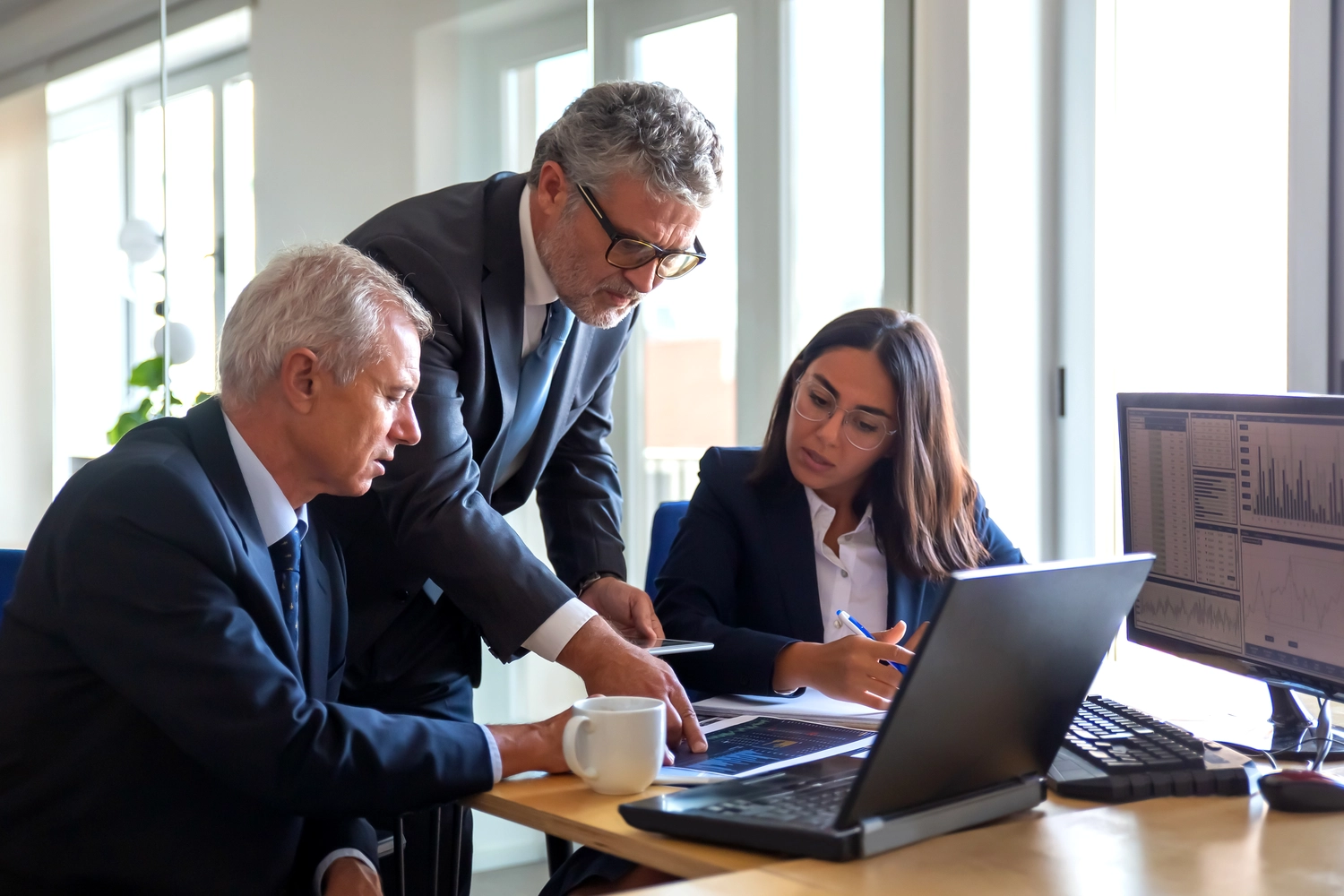 Mes West GmbH - Fachkräfte-, Investitions- und Unternehmenslösungen - Eine Büroszene mit drei Berufstätigen – zwei Männern und einer Frau –, die gemeinsam konzentriert auf einen Bildschirm schauen.