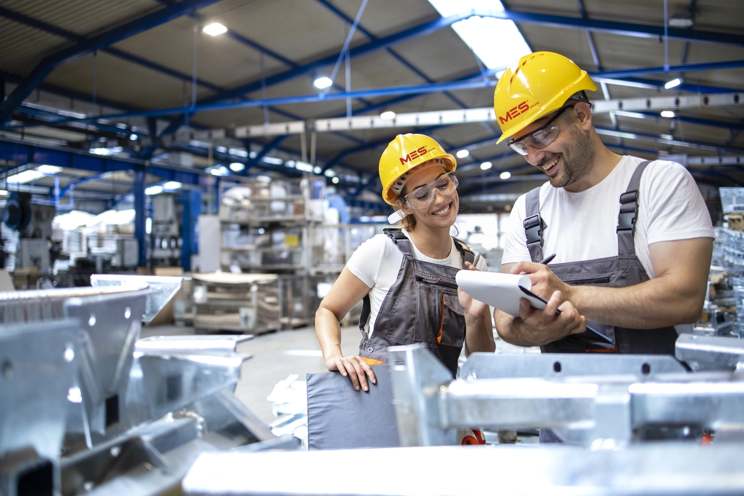 Mes West GmbH - Fachkräfte-, Investitions- und Unternehmenslösungen - Zwei Arbeiter in Schutzkleidung besprechen ein Dokument in einer Industrieanlage.